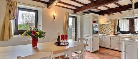 A dining area with a table set for four, a kitchen with white cabinets, and a stone wall.