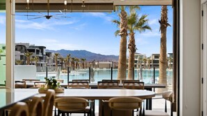 Un espace repas offrant une vue sur une piscine et des palmiers, avec en toile de fond un paysage montagneux.