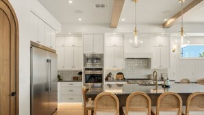Une cuisine moderne avec des meubles blancs, des appareils en acier inoxydable et un îlot central doté de chaises.