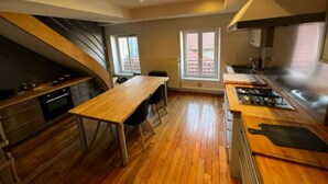 A modern kitchen with a wooden dining table, built-in appliances, and a large window providing natural light. - Le Grand Stanislas, 130 m2 Hypercentre 2/6 Pers (Nancy)