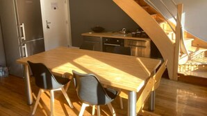 A modern kitchen with a wooden table and chairs, a built-in oven, and a staircase leading to an upper level. - Le Grand Stanislas, 130 m2 Hypercentre 2/6 Pers (Nancy)