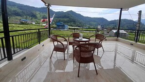 A covered outdoor area with a table and chairs, a view of green hills and a flag in the background. - York  Air Home (Kathmandu)