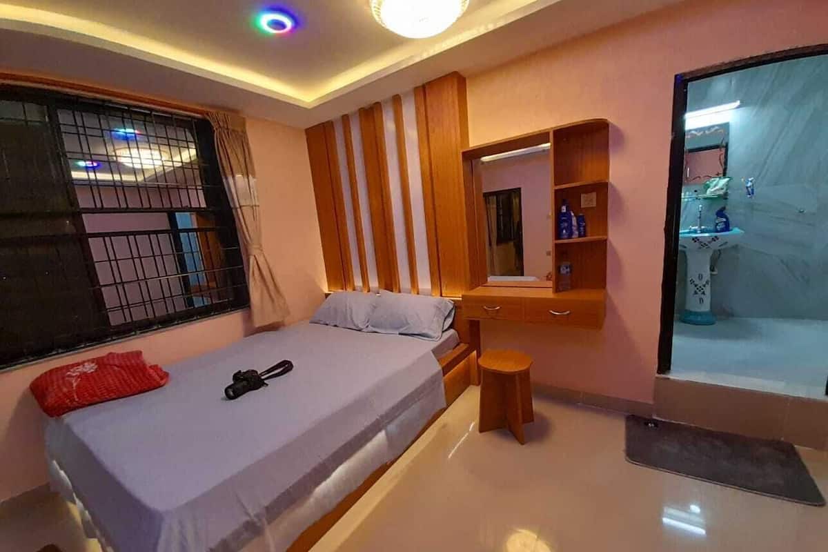 Ein Schlafzimmer mit einem Bett, einem kleinen Hocker, einem Schminktisch mit Spiegel und einem durch eine offene Tür einsehbaren Badezimmer.