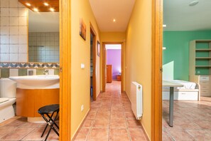 A narrow hallway with a bathroom on the left, a radiator on the right, and a bed in the background.