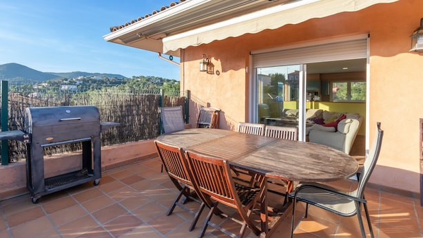 Une terrasse extérieure avec une table et des chaises, un barbecue et une porte-fenêtre coulissante donnant sur un espace intérieur.