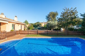 A swimming pool with a wooden deck and a fence, surrounded by trees and buildings.