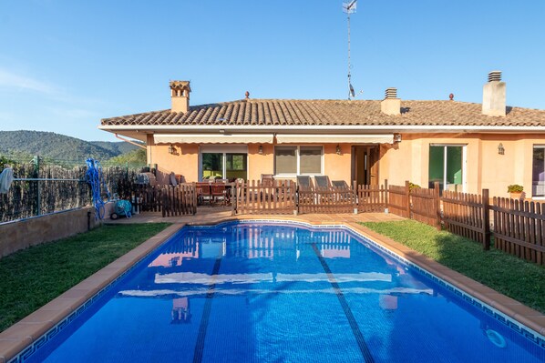 A residential property with a swimming pool, a fenced backyard, and a house with a tiled roof.