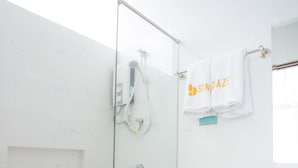A modern bathroom with a glass-enclosed shower, a white toilet, and a sink with a marble countertop. - Sundaze Dormitel (Naga)