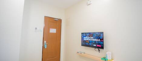 Una habitación de hotel con cama, televisión montada en la pared, estante de madera con libros y una puerta.
