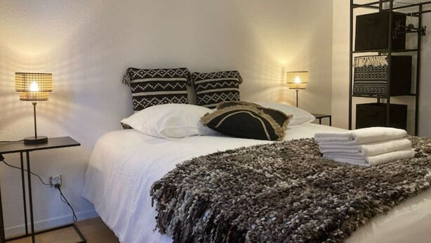 Un lit bien fait, agrémenté d’oreillers à motifs, d’un plaid et de deux lampes de chevet.