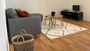 Un salon avec un canapé gris, une petite table en bois, un meuble pour la télévision et trois œuvres d’art encadrées accrochées au mur.