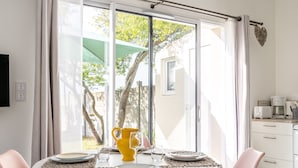 Un coin repas avec une table dressée pour deux personnes, un pichet jaune et une vue sur l’extérieur grâce à de grandes fenêtres.
