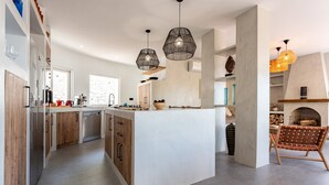 Une cuisine moderne dotée d’un îlot central, de luminaires suspendus et d’une cheminée.