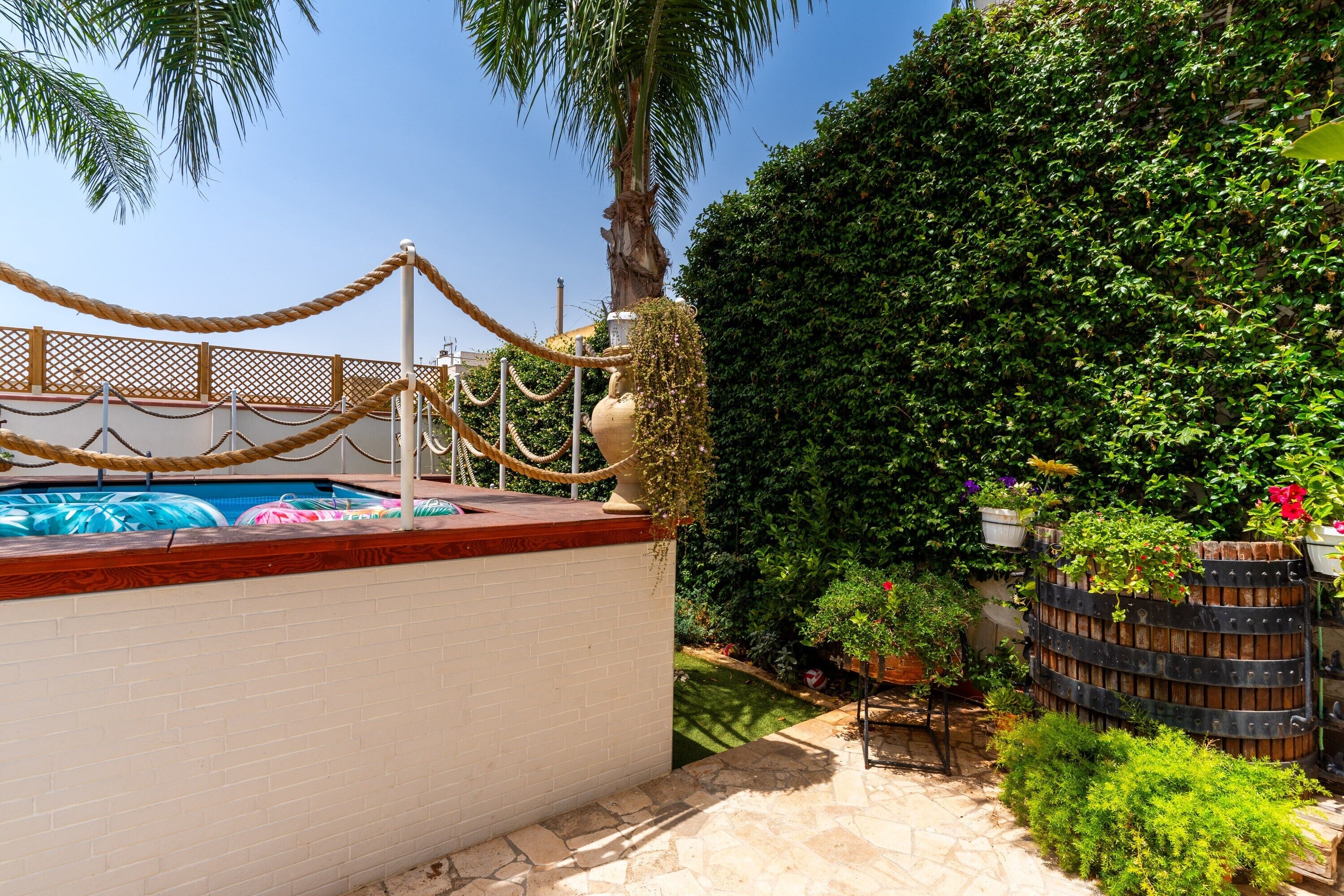 A pool with a rope barrier, a palm tree, and a hedge.