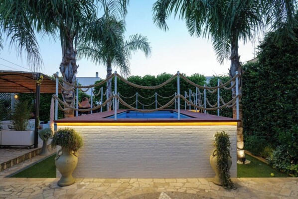 A swimming pool with a rope barrier, surrounded by palm trees and a brick wall.