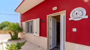 A red building with a sign reading 'Luxury Apartment Aurora' and a door open to the entrance.