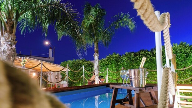 A pool area with a rope barrier, a table with a bucket and glass, and palm trees.