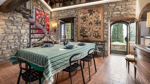 A rustic dining area with a stone wall, a table with a green tablecloth, and a large framed artwork. - Villa 'La Petrosa' with Private Pool, Private Garden and Balcony (Radda in Chianti)