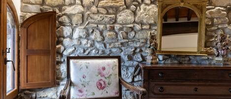 A room with a stone wall, a wooden cabinet, a floral upholstered chair, and a wooden dresser with drawers.