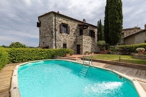 A stone building with a swimming pool, wooden deck, and a tall tree. - Villa 'La Petrosa' with Private Pool, Private Garden and Balcony (Radda in Chianti)