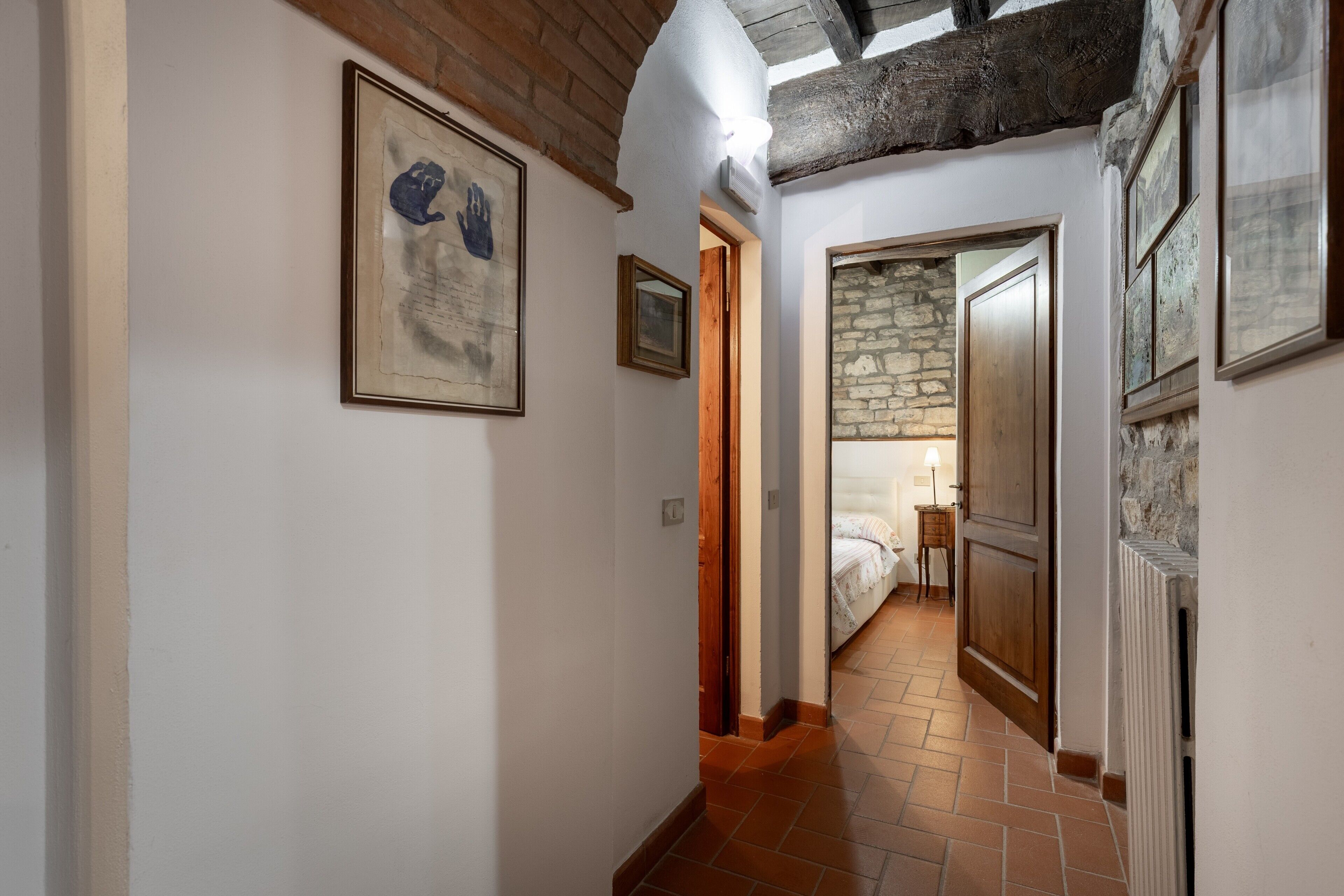 A hallway with a stone wall, a bed in the background, and a framed artwork on the wall.
