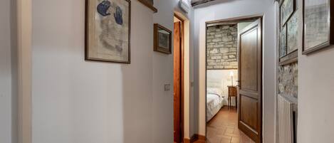 A hallway with a stone wall, a bed in the background, and a framed artwork on the wall.