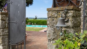 A gated entrance with a stone pillar, a metal gate, a bell, and a flower pot. - Villa 'La Petrosa' with Private Pool, Private Garden and Balcony (Radda in Chianti)