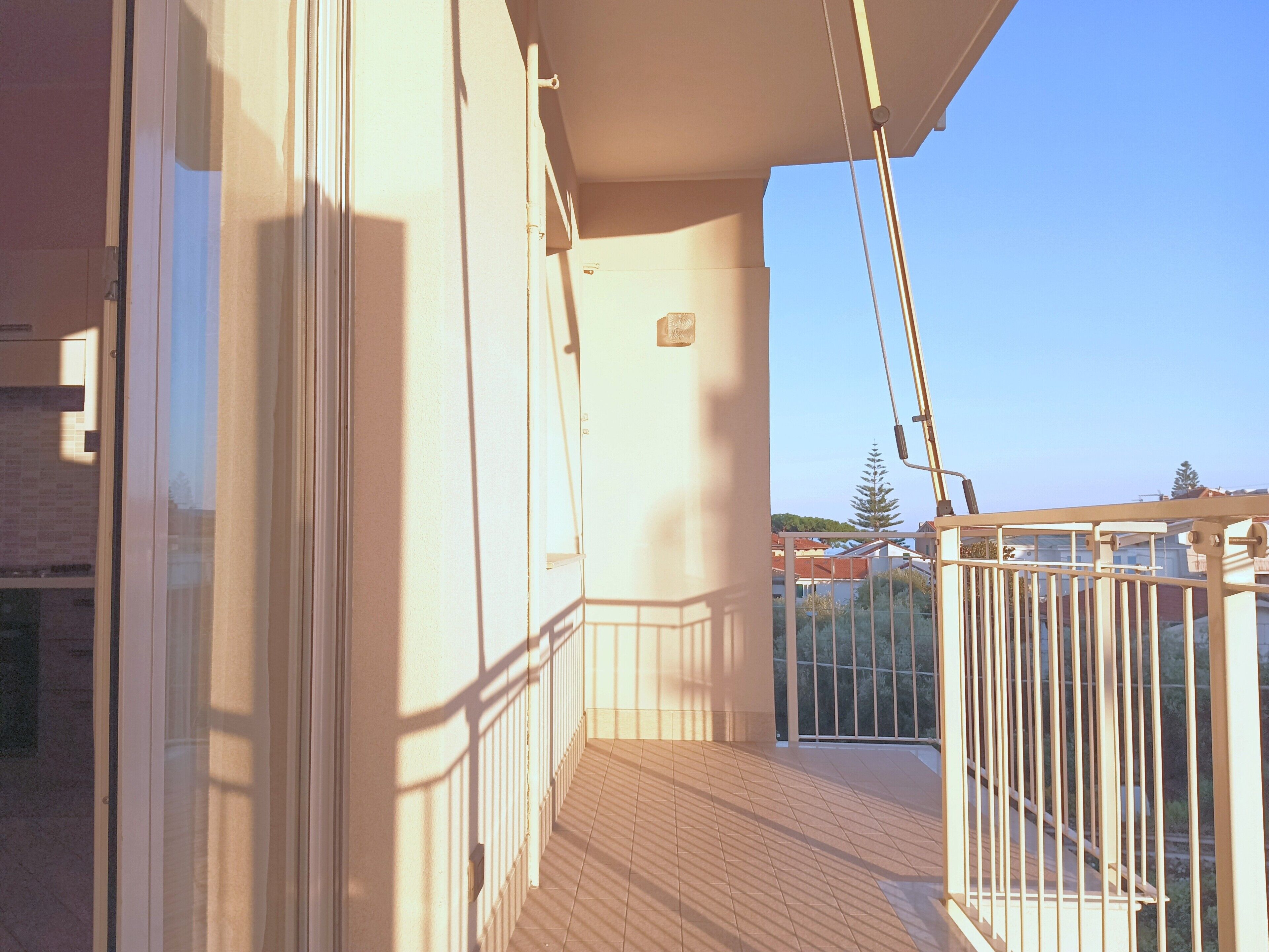 Un balcon doté d’un plancher en bois, d’une rambarde en métal et offrant une vue dégagée sur les bâtiments et les arbres environnants.
