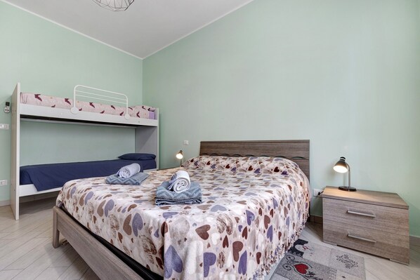 A bedroom with bunk beds, a bedside table with a lamp, and a patterned bedspread.