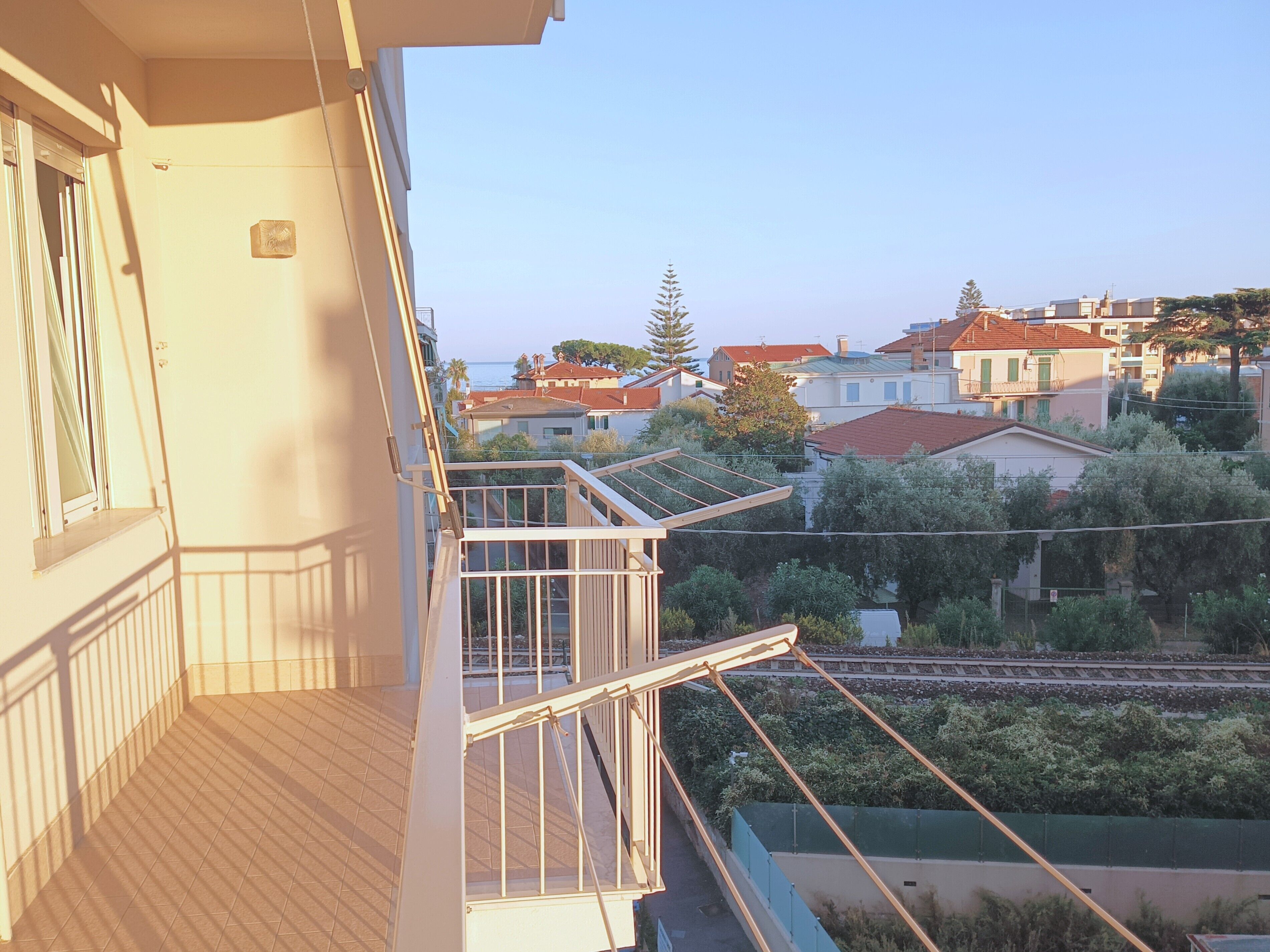 Un balcon donnant sur des immeubles d’habitation et un arbre.