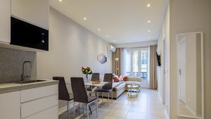 A modern kitchen with a built-in microwave, a dining area with a table and chairs, a sofa, and a large window with curtains.