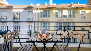 A balcony with a table set for breakfast, including croissants and a teapot, overlooking a row of buildings with balconies.