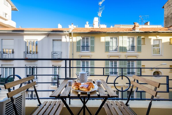 A balcony with a table set for breakfast, including croissants and a teapot, overlooking a row of buildings with balconies. - Holiday Apartment "Sea View" near Beach with Balcony & Wi-Fi (Nice)