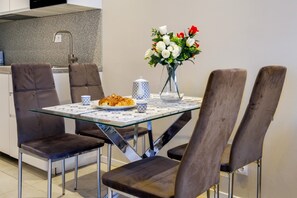 Un coin repas avec une table en verre, quatre chaises, un vase avec des fleurs, un croissant et une théière.