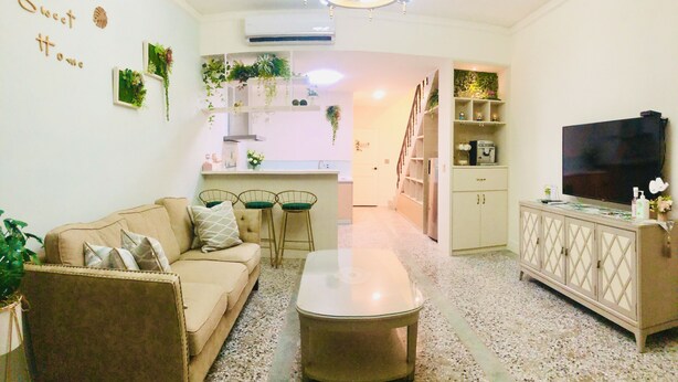 A living room with a sofa, coffee table, and TV. There are plants on the walls and a kitchen in the background. - 6 person single house (Taitung)