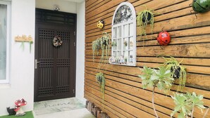 A wooden house with a dark brown door, a window with decorative ironwork, and various plants and ladybug decorations on the exterior wall. - 6 person single house (Taitung)