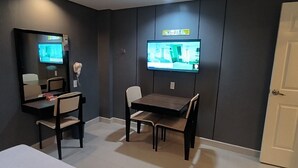 A room with a dark-colored wall, a flat-screen TV mounted above a wooden table and two chairs, a hairdryer, and a mirror on the left wall. - Hotel Sogo Davao (Davao)