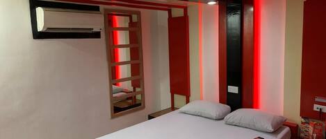 A hotel room with a bed, a bedside table with a phone, a wall-mounted air conditioner, and a red and white striped wall panel.