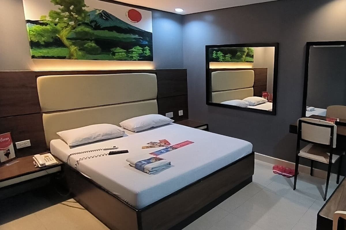 A modern hotel room with a large bed, bedside tables, a desk, and a chair. There are two mirrors on the walls and a painting above the bed.