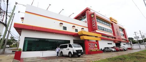 A hotel with a red and white facade, a large garage, and several parked cars.
