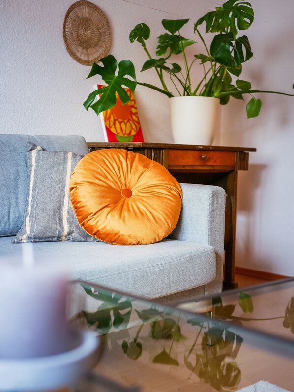 Un salon avec un canapé, un coussin rond orange, une plante en pot et une décoration murale.