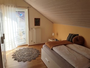 Une chambre à coucher comprenant un lit, une table de chevet, une lampe, un radiateur, une fenêtre avec des rideaux et une porte.