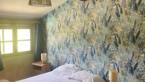 Een slaapkamer met een bed, twee nachtkastjes, een hanglamp en een raam met gordijnen.