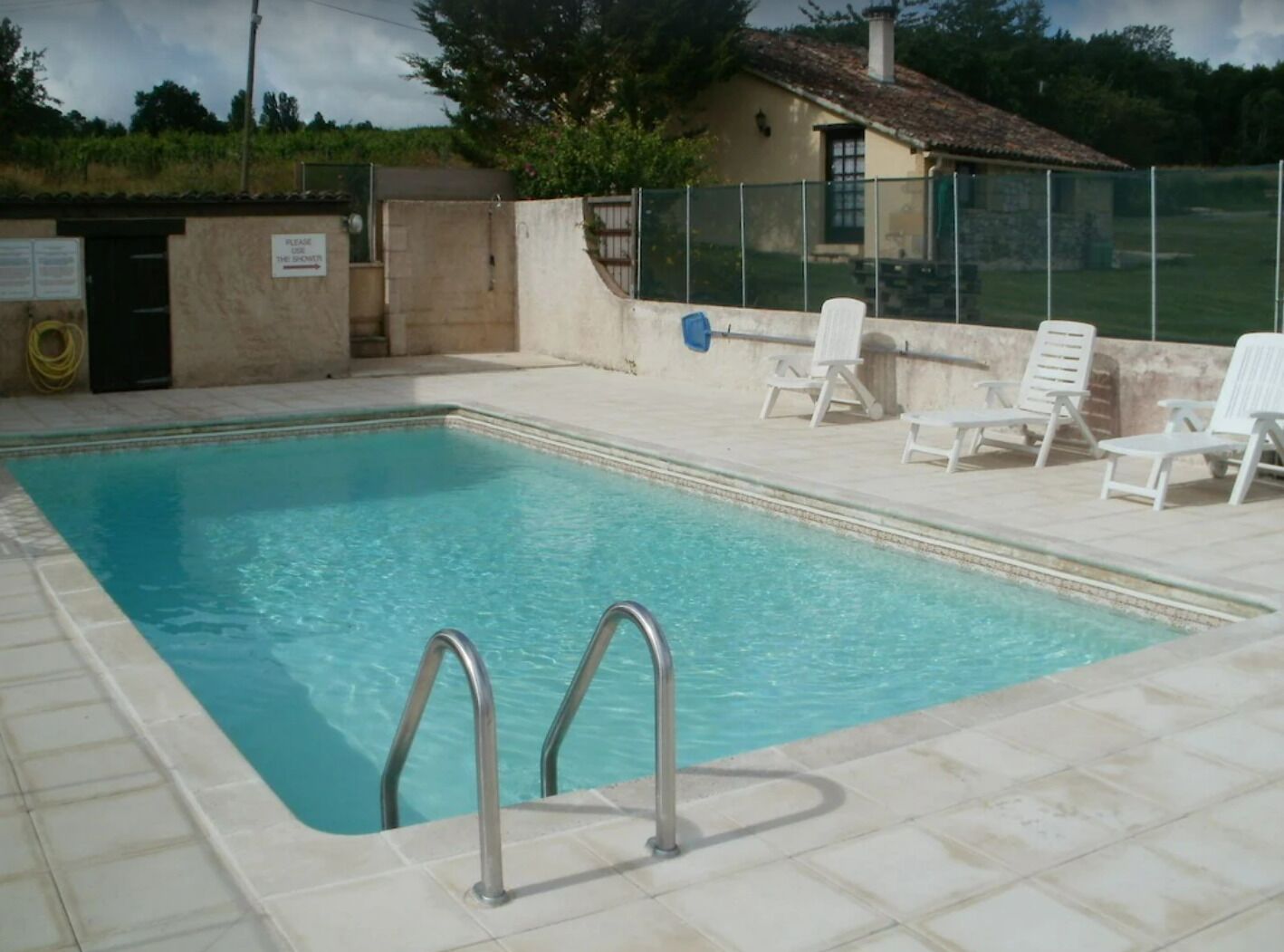 A rectangular swimming pool with a tiled deck, metal pool ladders, and white lounge chairs.