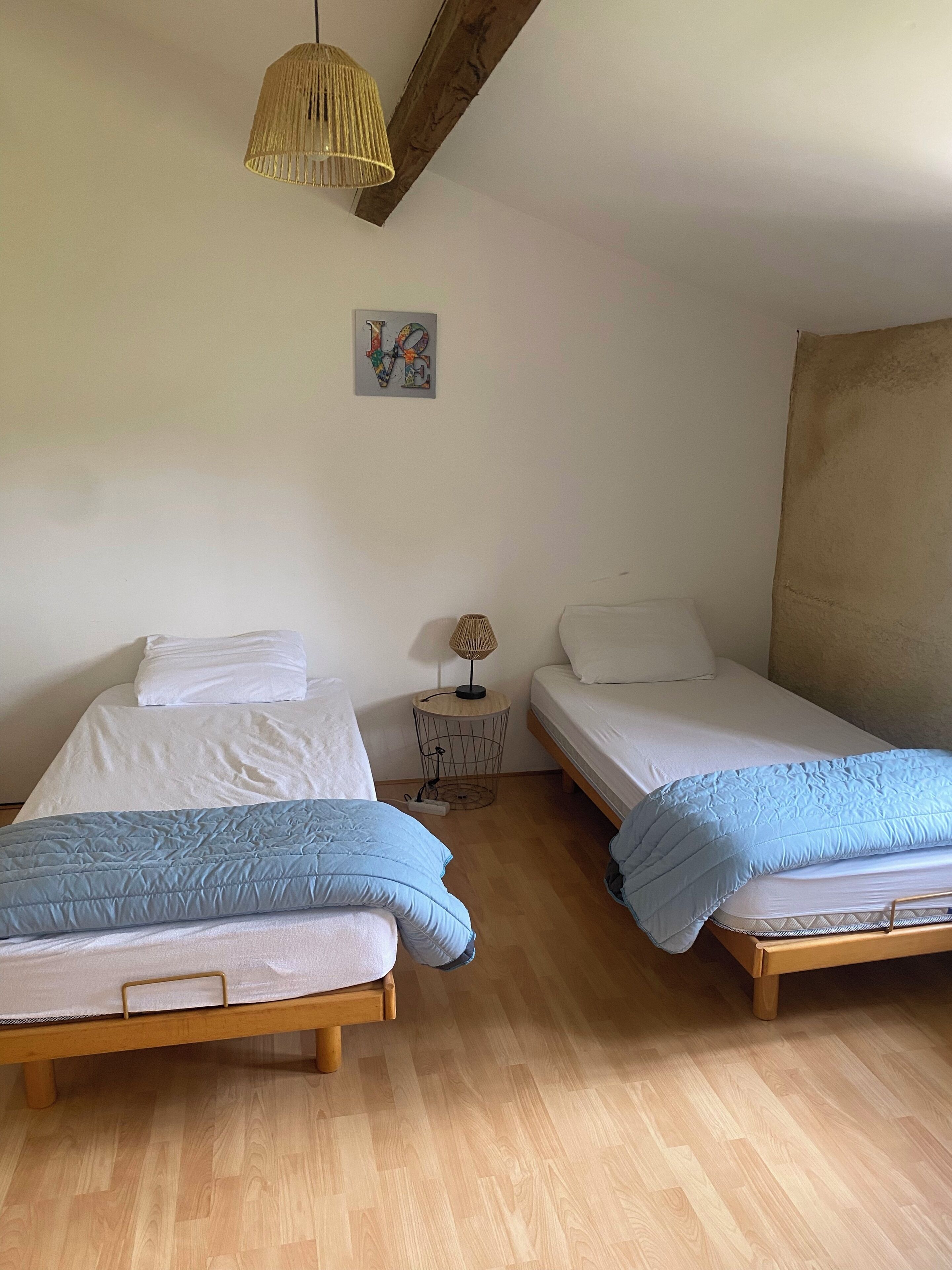 A room with two beds, a small table with a lamp, and a 'LOVE' decoration on the wall.
