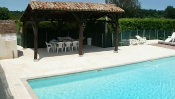 A swimming pool with a tiled deck, a covered seating area with tables and chairs, and a sign requesting the use of the shower.