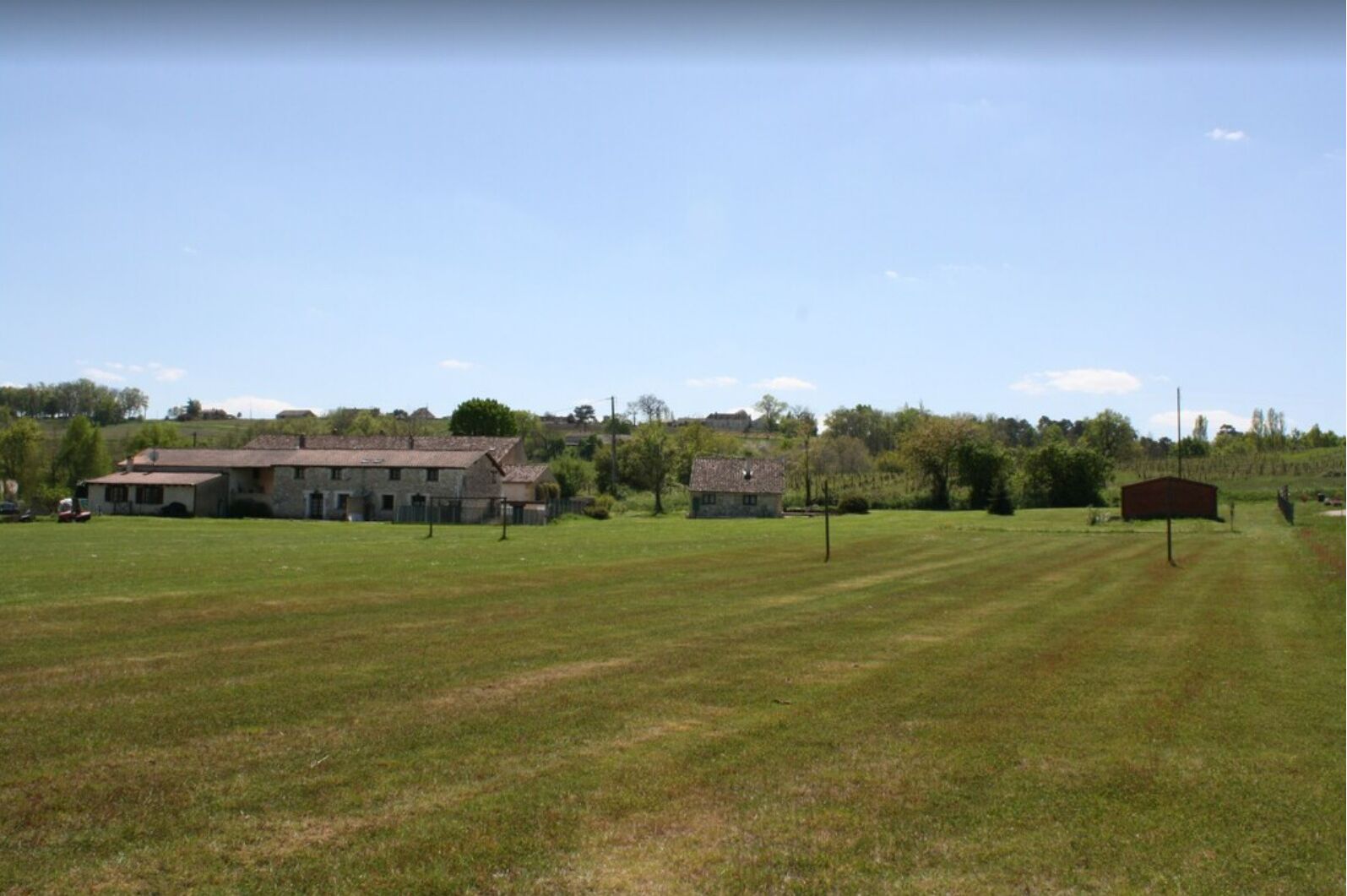Een landelijke omgeving met een groot open veld, een boerderij en een kleine schuur.