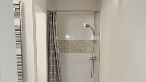 A small, modern shower area with a glass door, a showerhead, and a wall-mounted light fixture.
