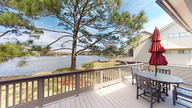 A deck with a table and chairs, overlooking a lake and a building. - Lakeside Updated Villa: Pool and Beach Access (Pawleys Island)