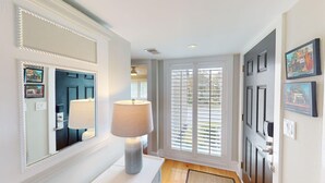 A hallway with a white console table, a lamp, a mirror, and a door with a window. - Lakeside Updated Villa: Pool and Beach Access (Pawleys Island)